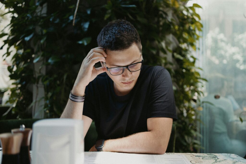 Man wearing glasses sitting at a table looking down thoughtfully, navigating the process of returning to teaching after living abroad
