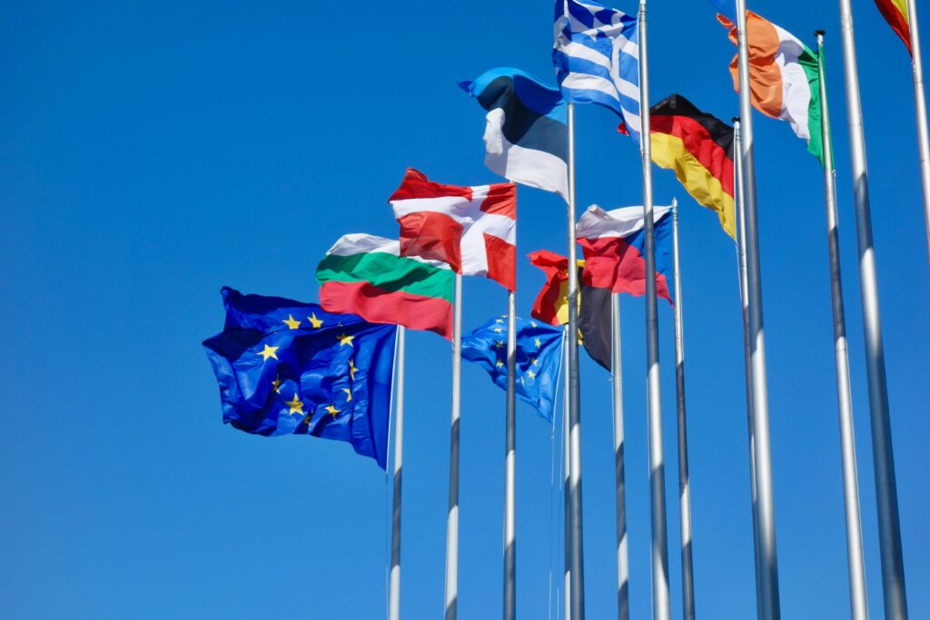 Multiple European country flags and EU flags flying against a blue sky — representing the range of teaching abroad salary options across Europe in a teaching abroad salary comparison
