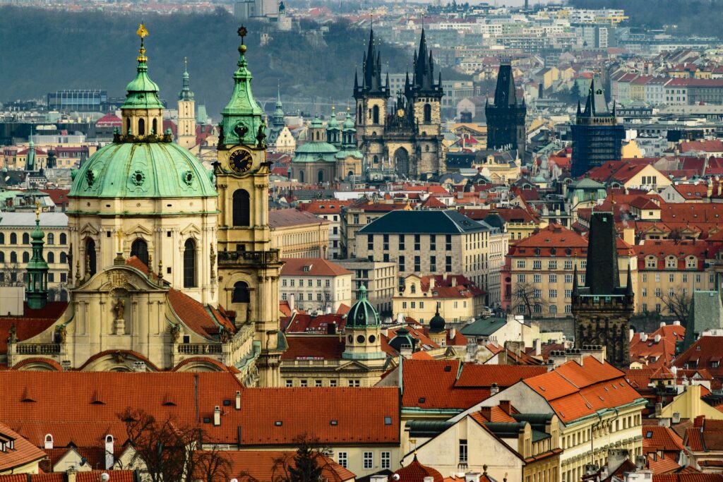 That's the Prague skyline — St. Nicholas Church with its green dome in the foreground, the Church of Our Lady before Týn's Gothic spires in the middle, and the red rooftops of Malá Strana stretching across the frame. Beautiful shot.