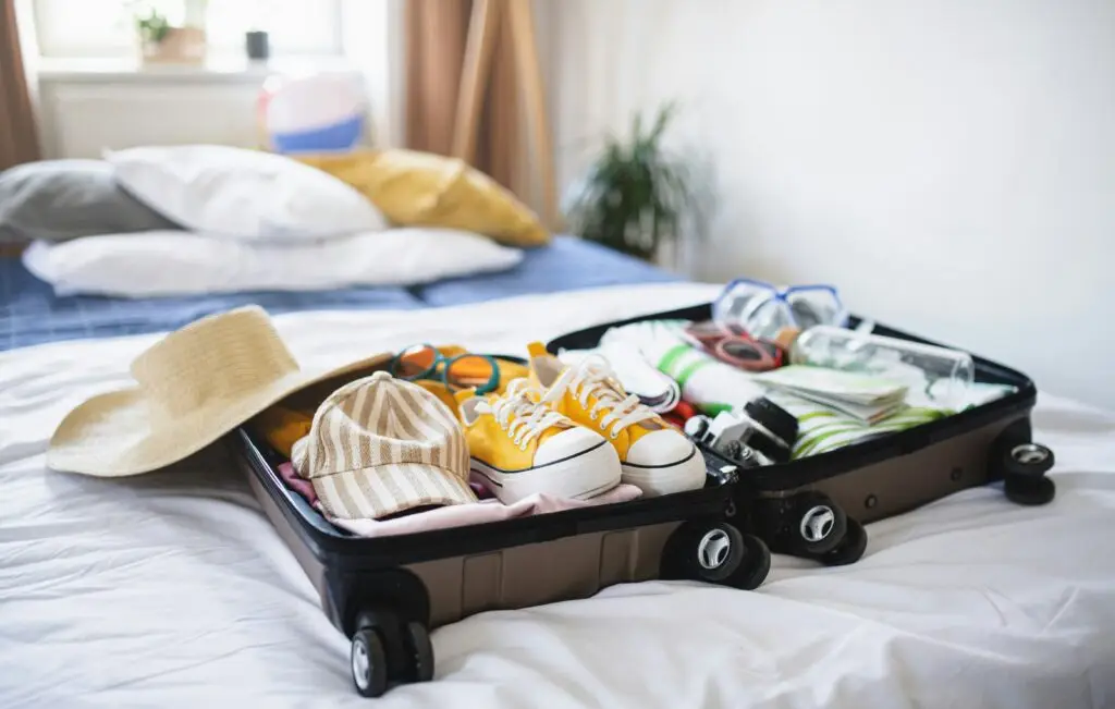 what to pack to teach abroad — packed suitcase with shoes, hat, and travel essentials on bed