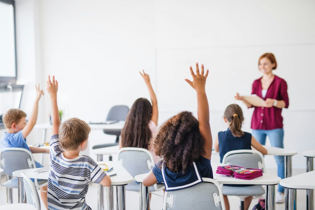 Students raising hands enthusiastically in an English classroom abroad with female teacher at the front