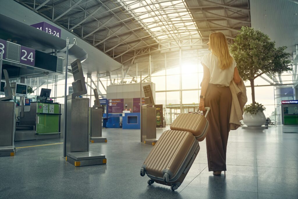 Woman walking through an airport terminal with luggage, seen from behind in golden light
