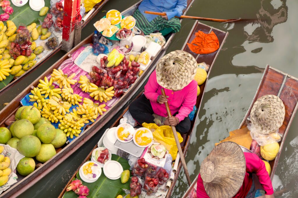 Aerial view of vendors in wooden boats selling tropical fruit at a floating market in Thailand — one of the vivid daily experiences for people who teach English in Thailand