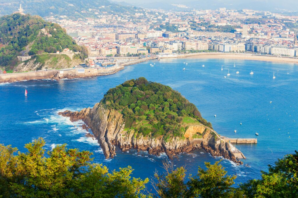 That's Santa Clara Island in La Concha Bay, San Sebastián — one of the most beautiful coastal views in Spain.
Alt text:
Aerial view of Santa Clara Island in La Concha Bay, San Sebastián, Spain, with the city's beach and coastline visible in the background