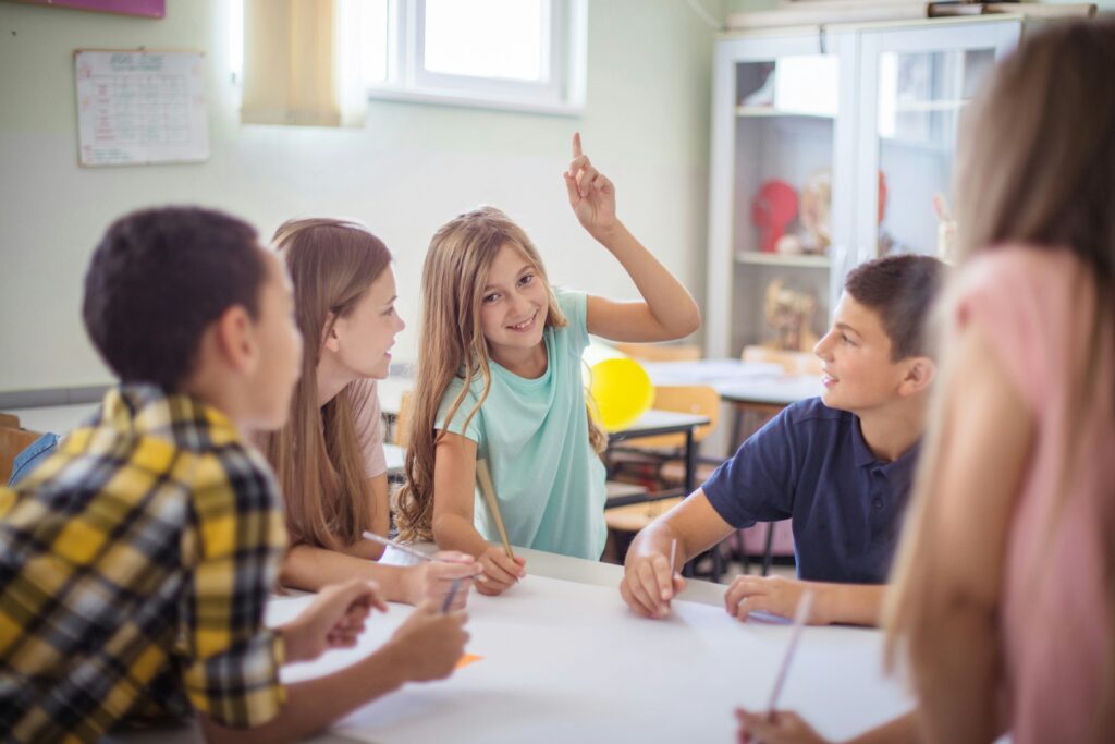 Students working together at a table in an international school classroom, one girl raising her hand