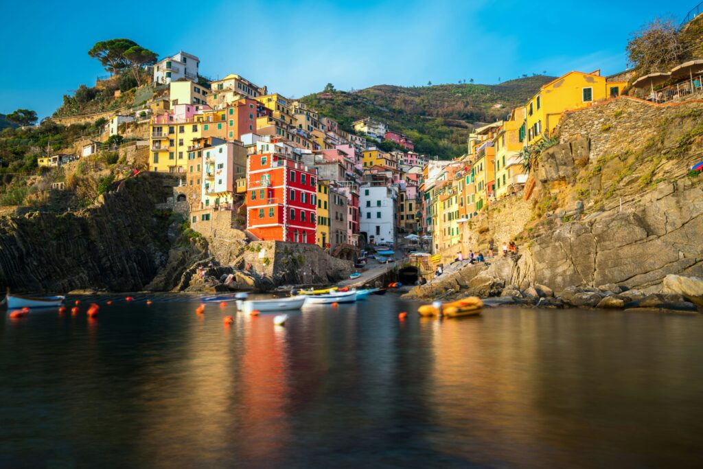 Colorful houses stacked on cliffs above a small harbor in Riomaggiore, Cinque Terre, Italy, with fishing boats on calm blue water