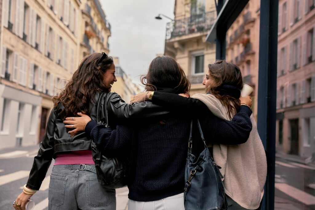 Three women friends walking arm in arm through a European city street after taking an in person TEFL course abroad together