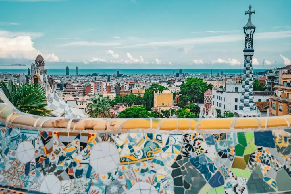View of Barcelona from the mosaic terrace of Park Güell, with Gaudí's colorful tilework in the foreground and the Mediterranean Sea in the distance