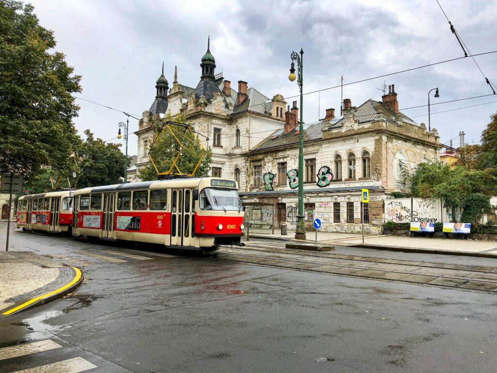 A vintage red tram passing weathered, graffiti-covered buildings on a quiet Prague street.