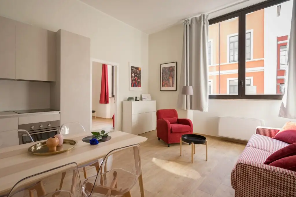 Cozy, furnished apartment living room with a red armchair, dining table, and city view — an example of a fully furnished rental.