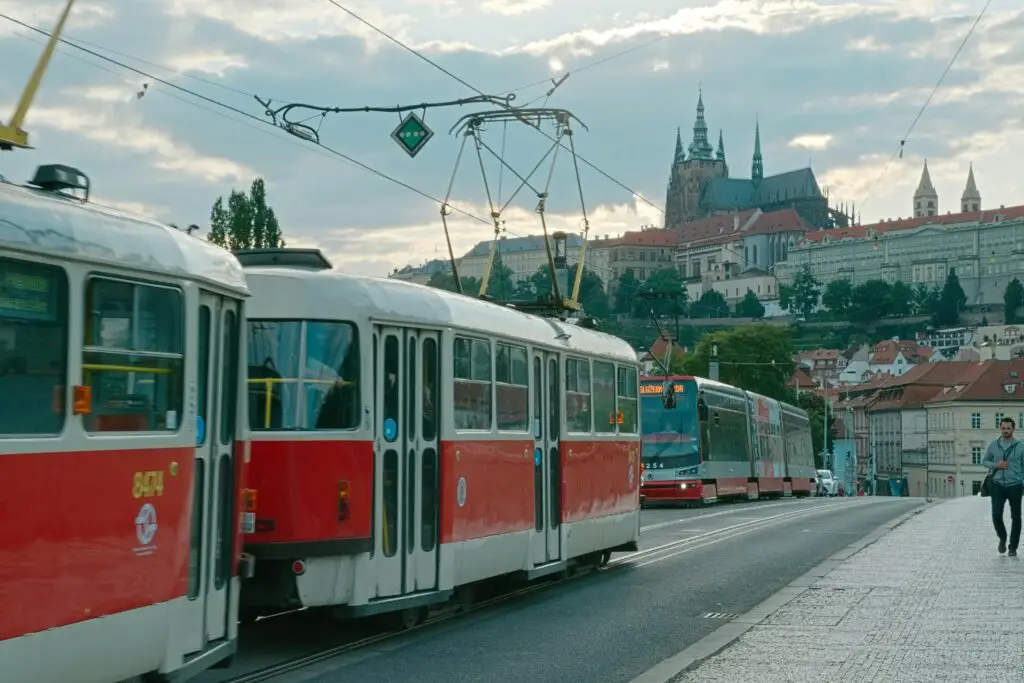 Two red and white trams on a Prague street with Prague Castle visible in the background, part of navigating public transportation in Prague.
