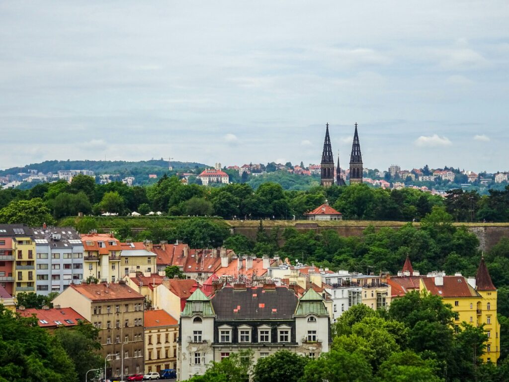 Prague residential skyline with red-tiled rooftops, church spires, and green hills, showing the neighborhoods where locals and expats actually live.