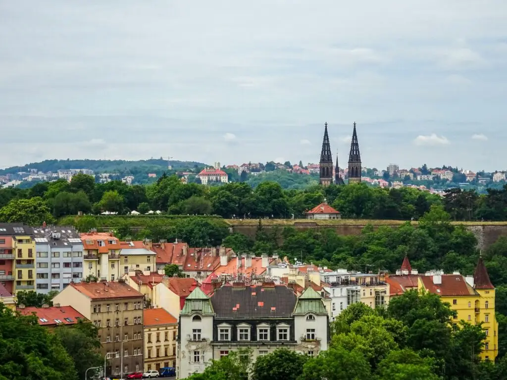 Prague residential skyline with red-tiled rooftops, church spires, and green hills, showing the neighborhoods where locals and expats actually live.