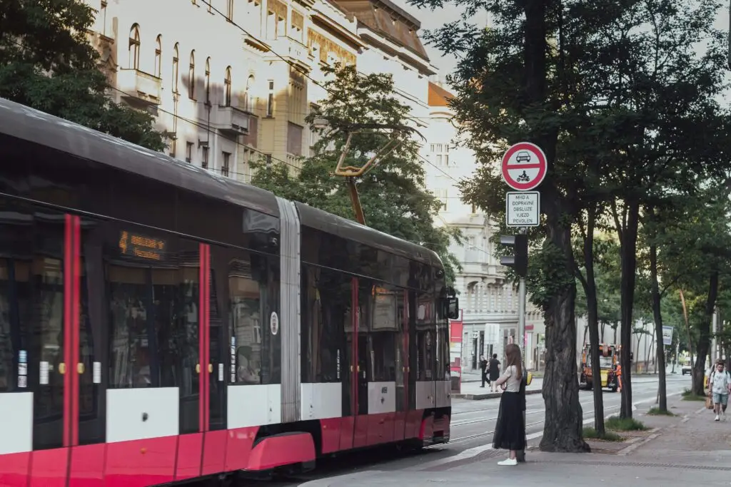 Modern Prague tram stopped at a platform with a woman waiting, part of navigating public transportation in Prague.