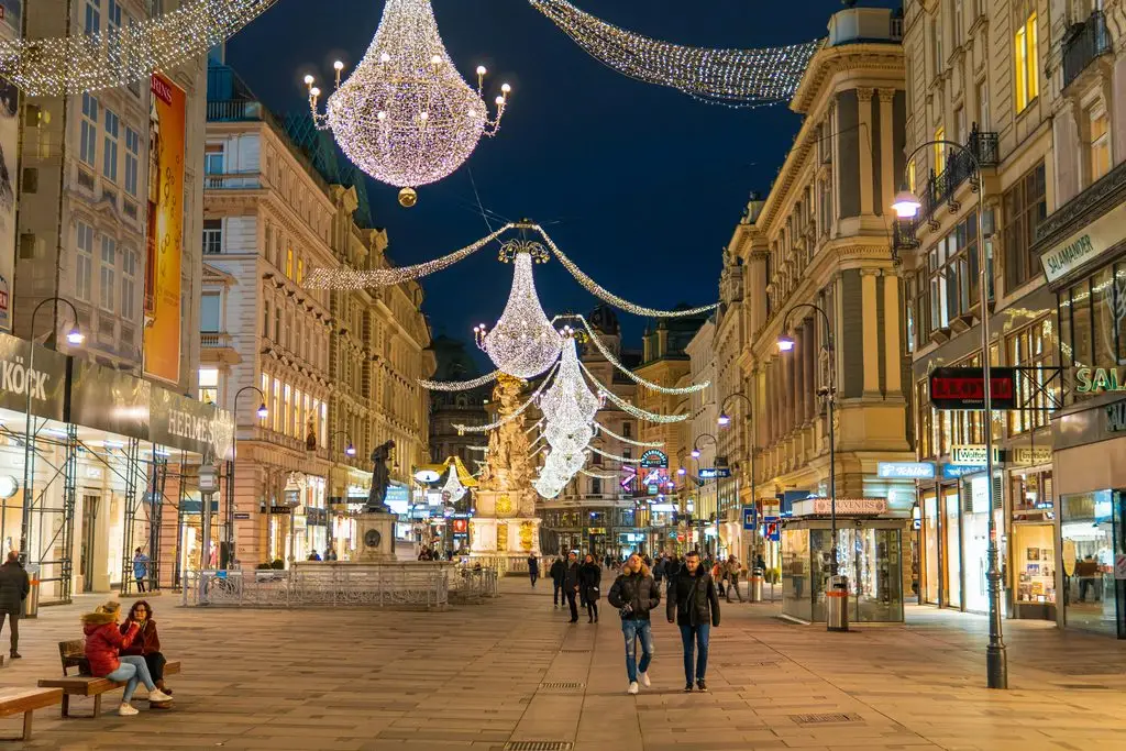 Vienna travel guide: the Graben shopping street at night, lit with chandelier-style holiday lights above shoppers.
