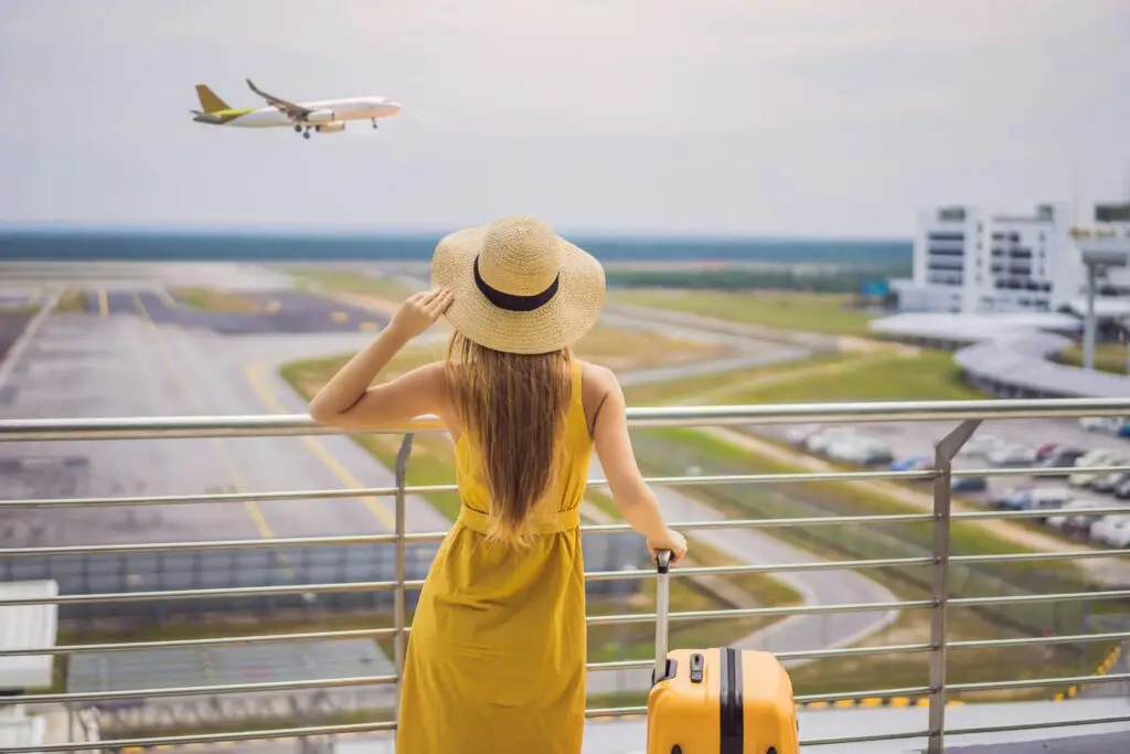 Woman with a yellow suitcase watching a plane take off from an airport observation deck
