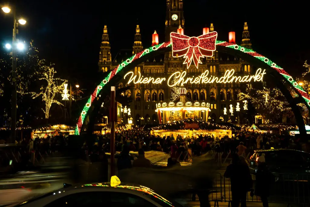 Vienna travel guide: lit-up Wiener Christkindlmarkt entrance arch at Rathausplatz, with City Hall glowing behind the crowd.