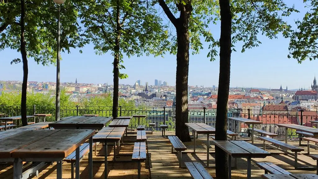 Empty picnic tables under chestnut trees at Letná Beer Garden, overlooking Prague's rooftops and skyline.