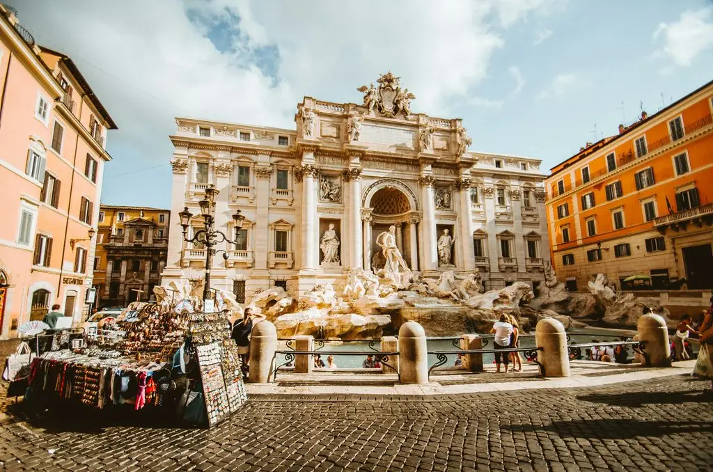 The Trevi Fountain in Rome, with souvenir stalls and crowds on a sunny day.