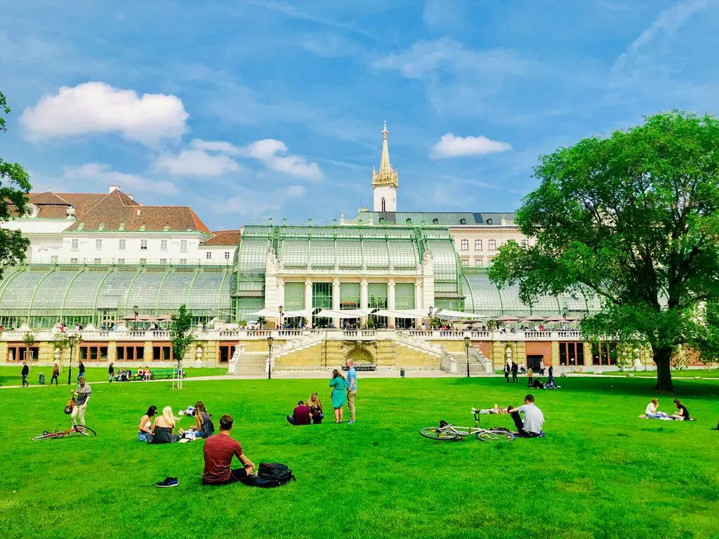 Week-long spring break destinations in Europe: locals relax on the lawn at Burggarten in Vienna, with the Palm House behind them.